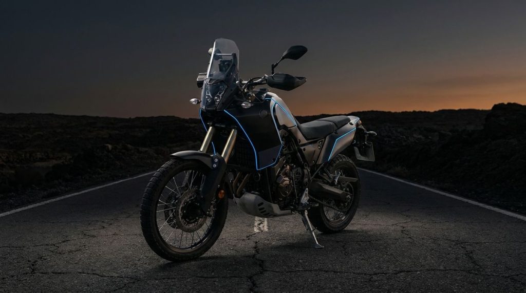 Trail routier adventure-touring bridable A2 sur route déserte au crépuscule, ambiance charbon et accent bleu électrique.